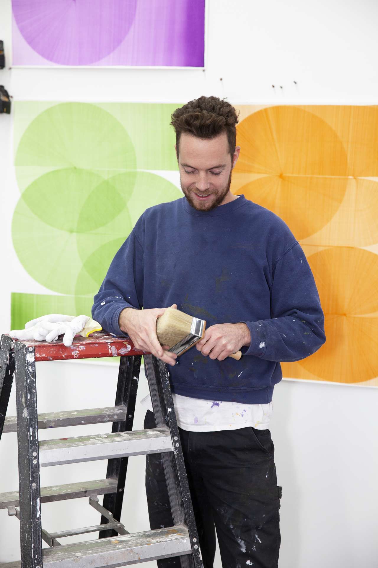 man heeft verfkwast vast en leunt op trap in atelier met kunst