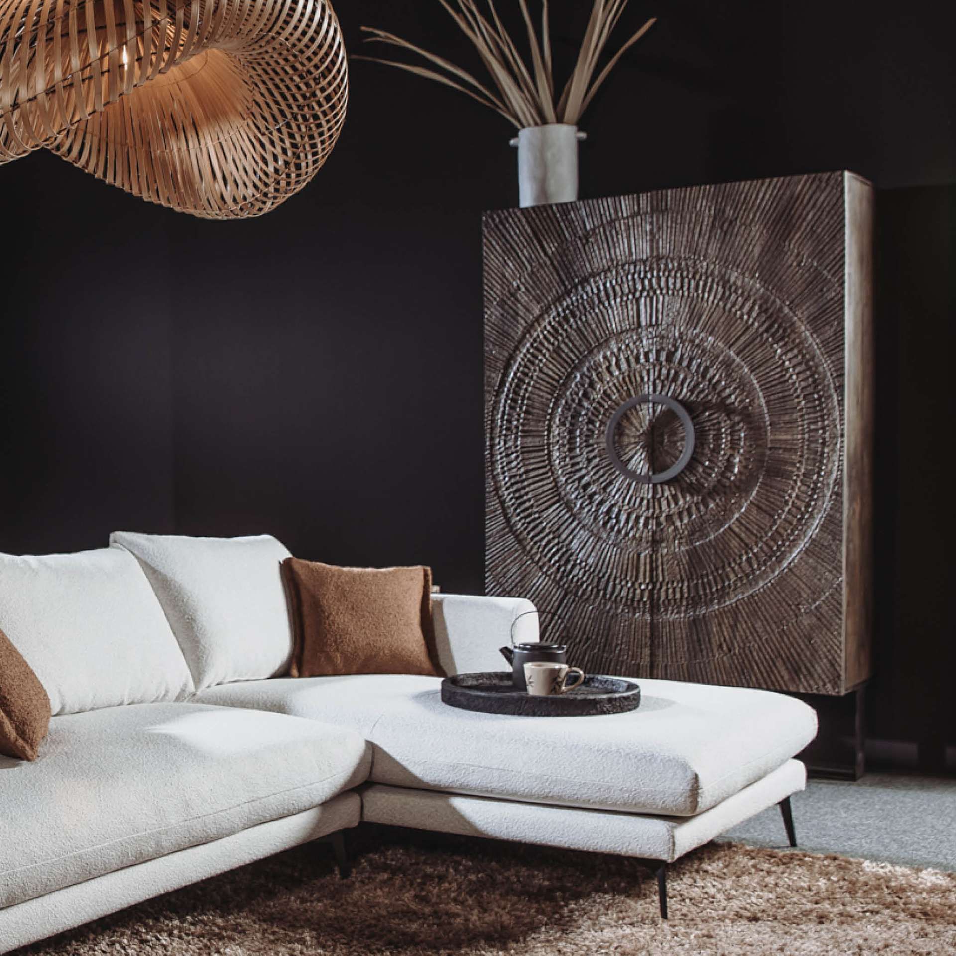 Hoge houten wandkast met houtsnijwerk met daarvoor een witte hoekbank