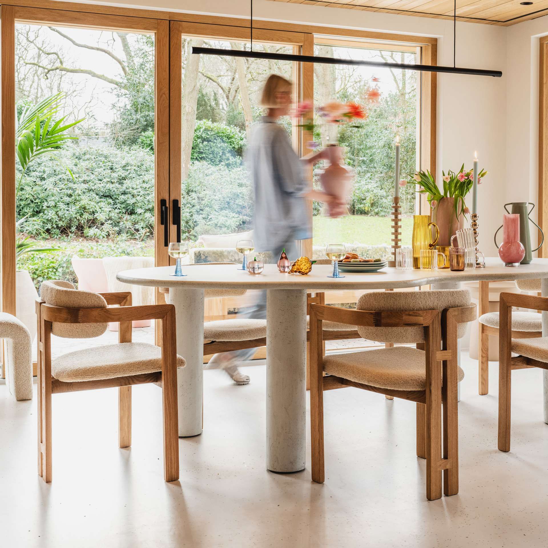 eetkamer met vrouw die langs loopt met een vaas bloemen in de handen