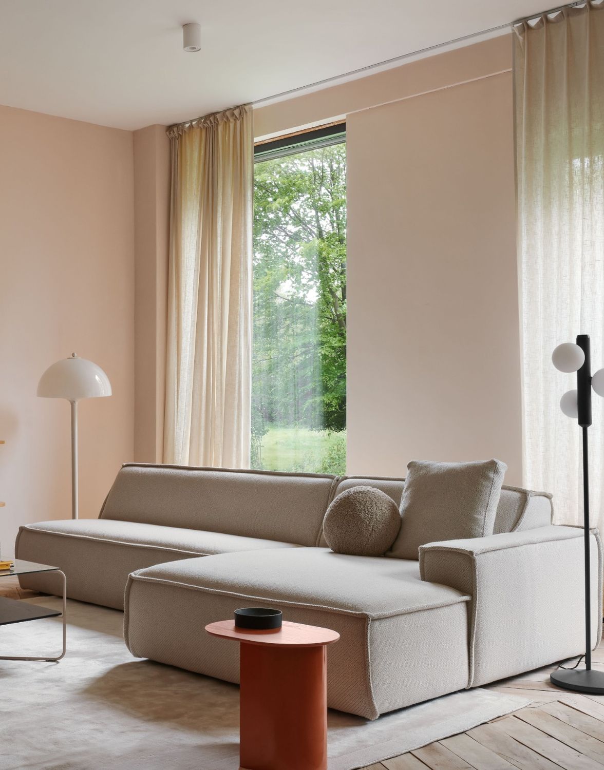 Beige bank in een licht ruimte met vloerlampen en een bijzettafel