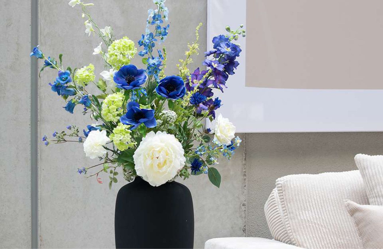 Blauwe kunstbloemen in zwarte vaas