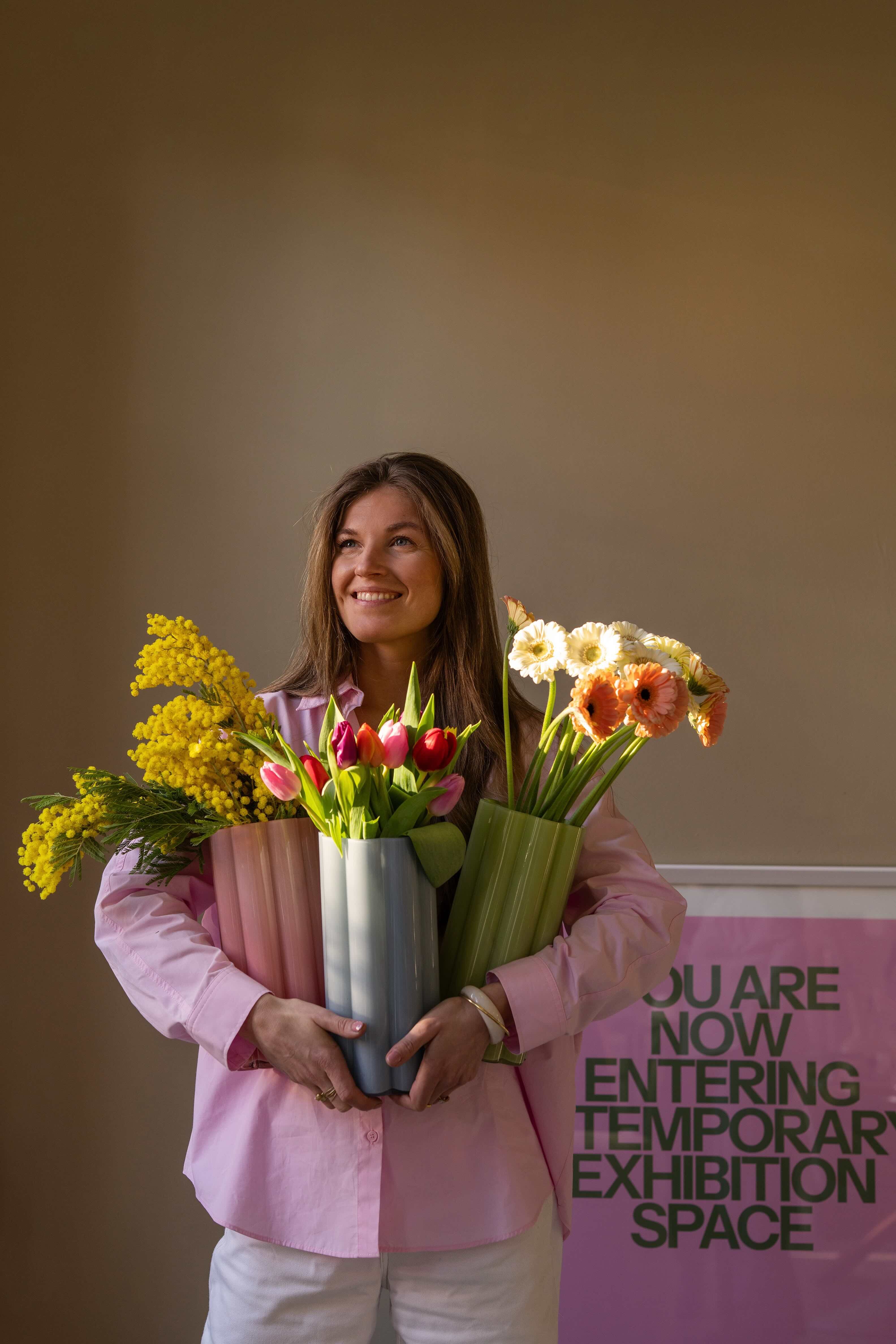 Vrouw met roze blouse en verschillende vazen bloemen in handen