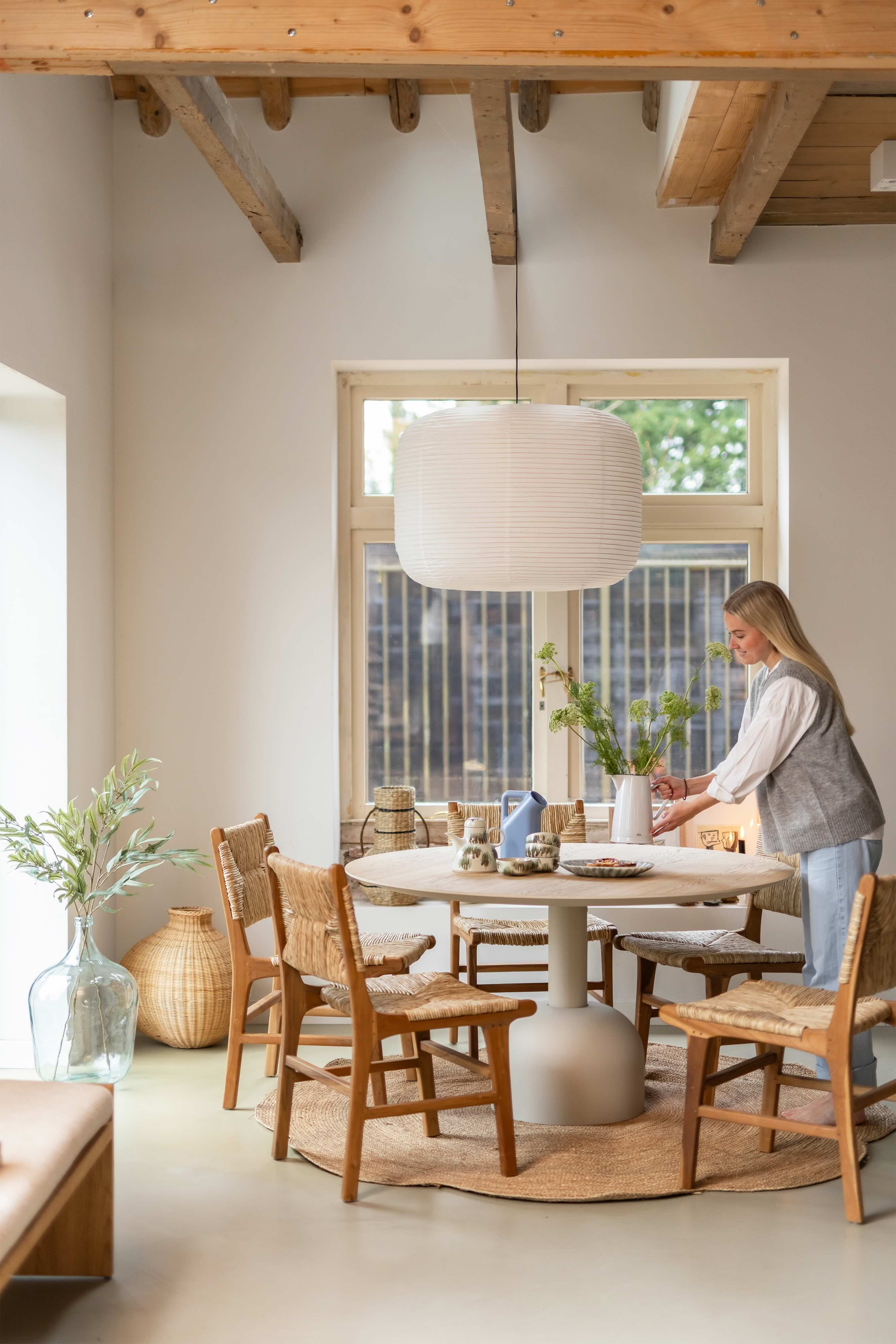 Lichte eettafel met houten stoelen vrouw die bloemen neerzet