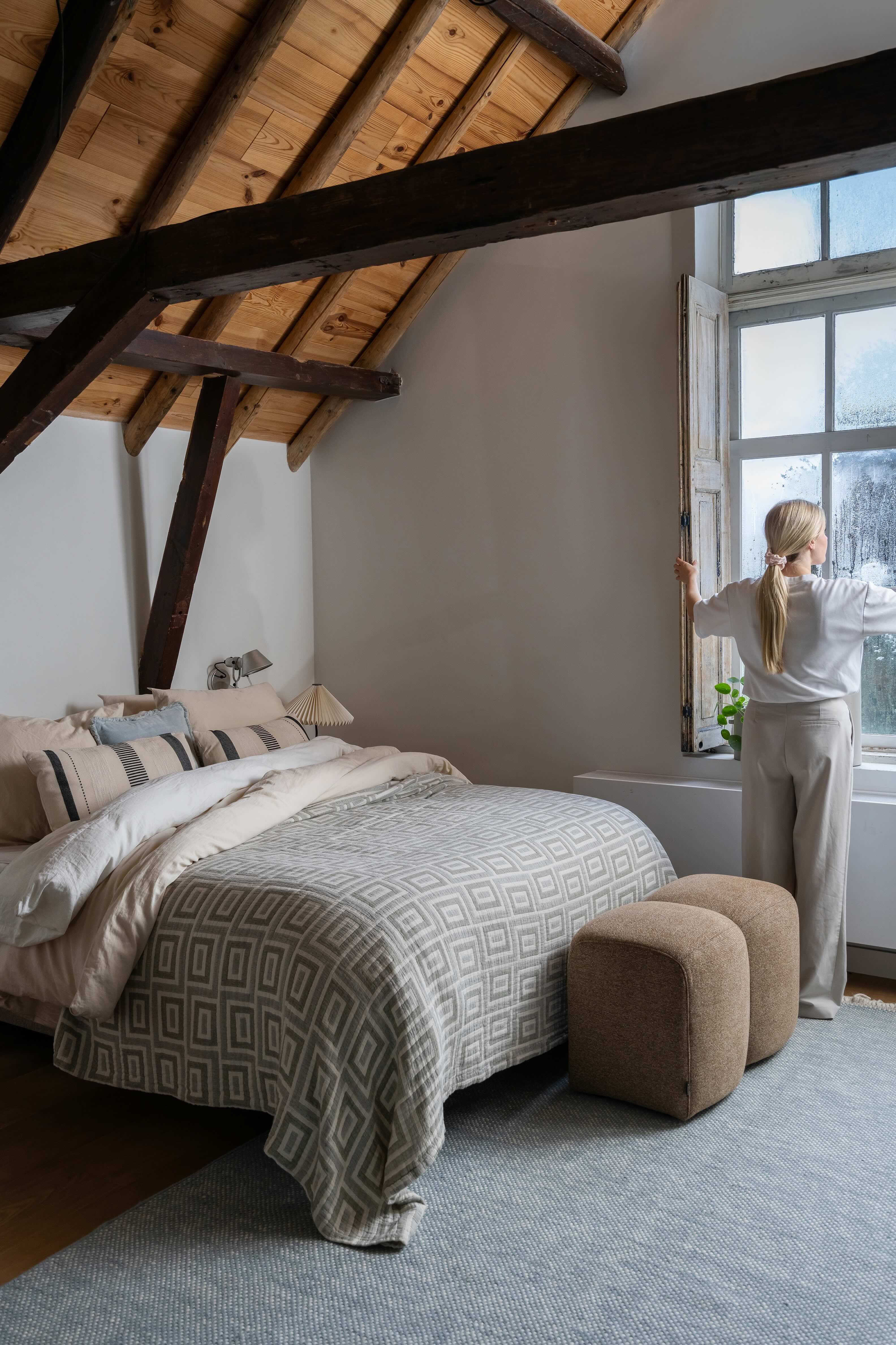 Bed met lichtbeddengoed en vrouw die bij het raam staat