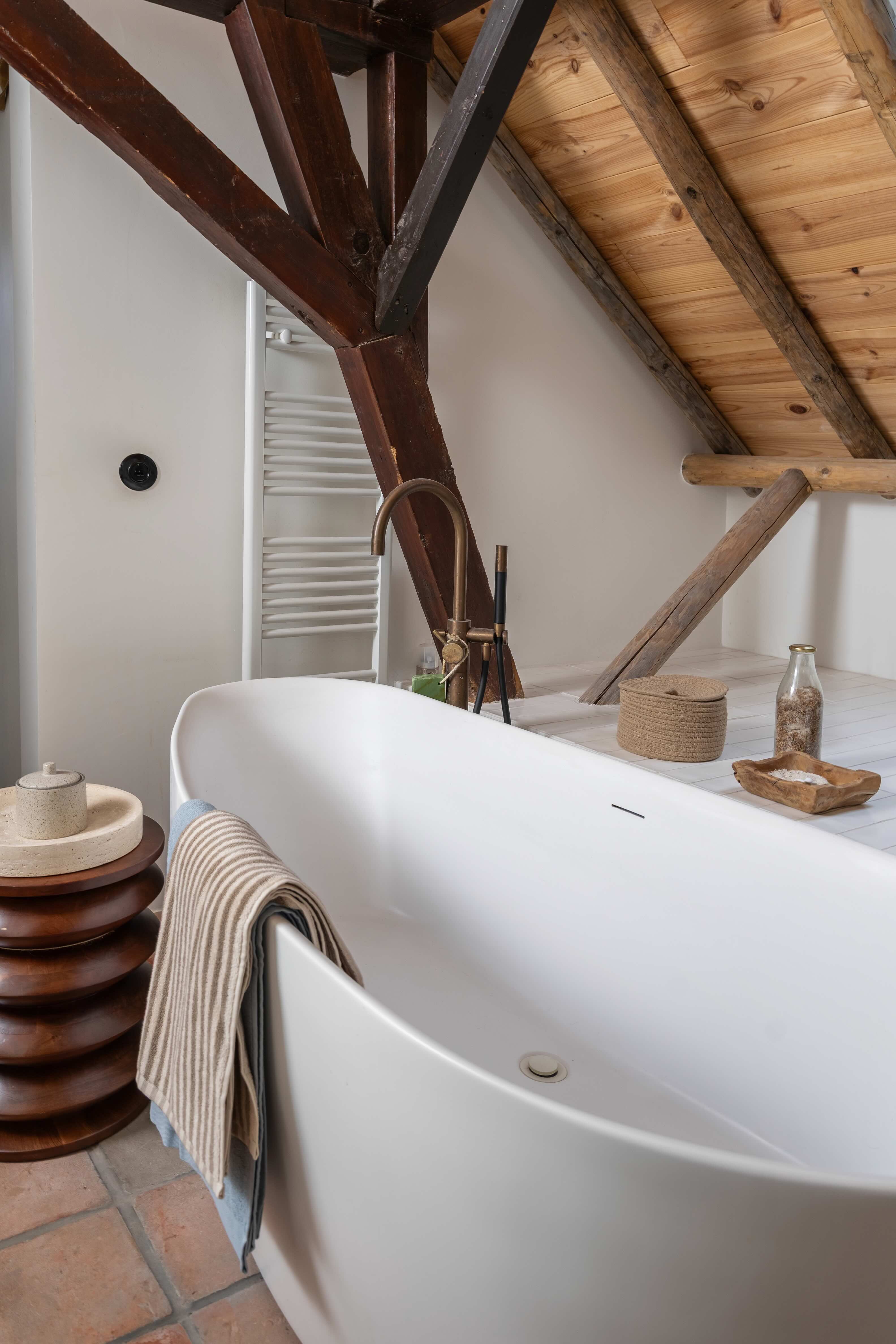 Groot wit bad in landelijke badkamer met houten balken