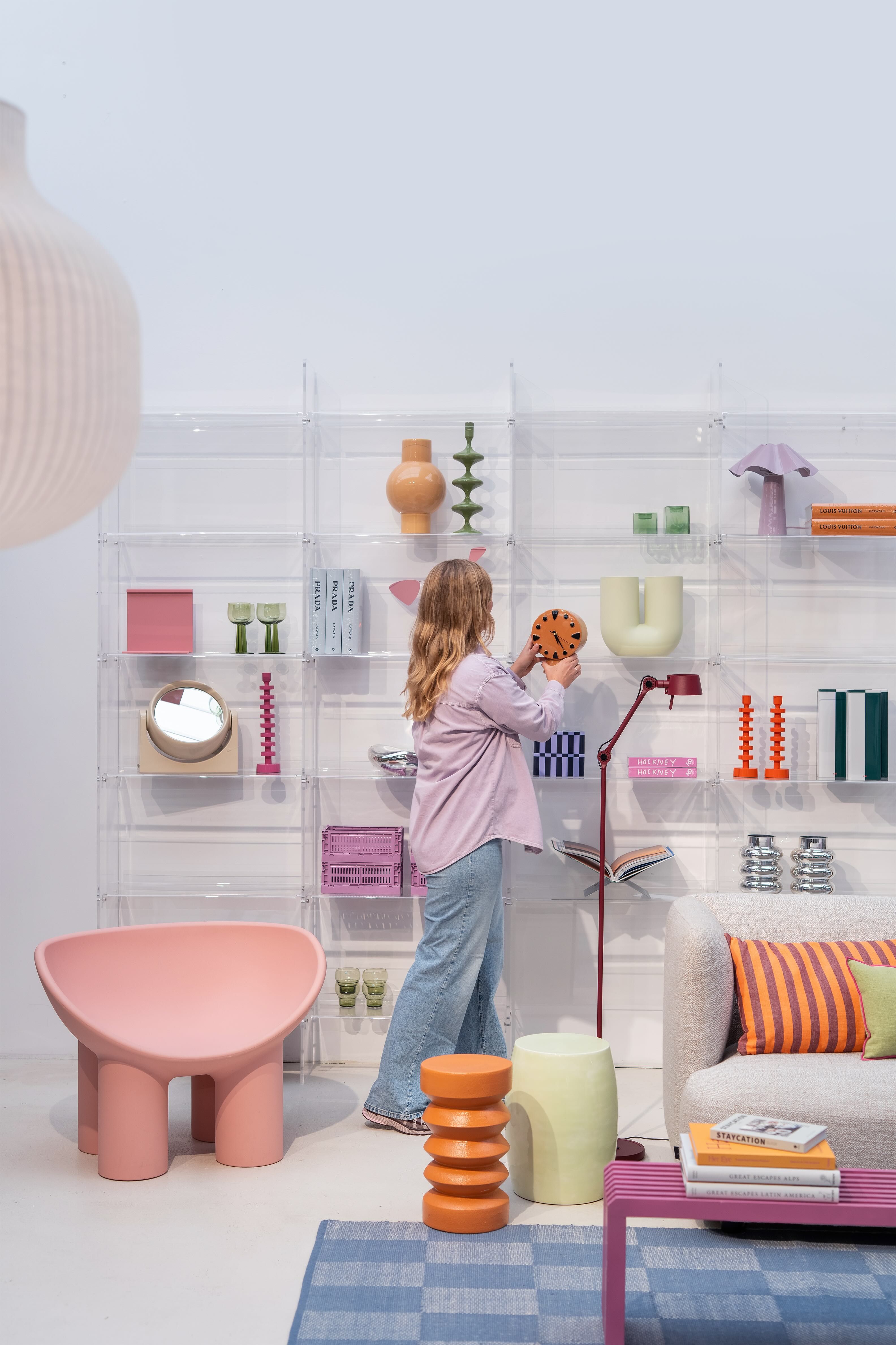 Stylist die wandkast inricht en een oranje klok vasthoudt