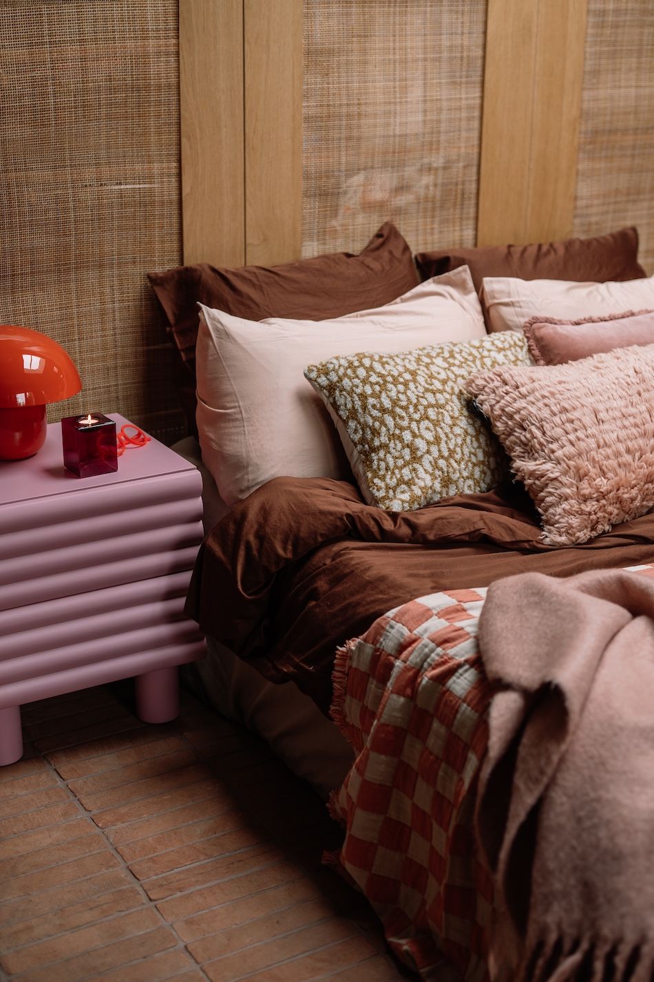 Opgemaakt bed met veel kussens en nachtkastje