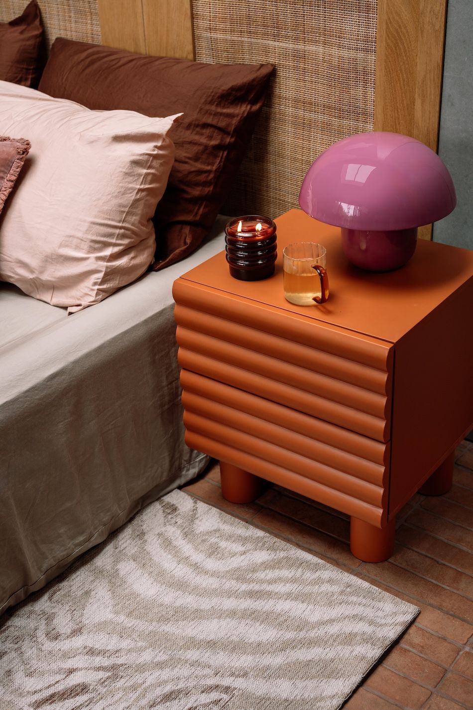 oranje nachtkastje met roze lamp, theeglas en kaars