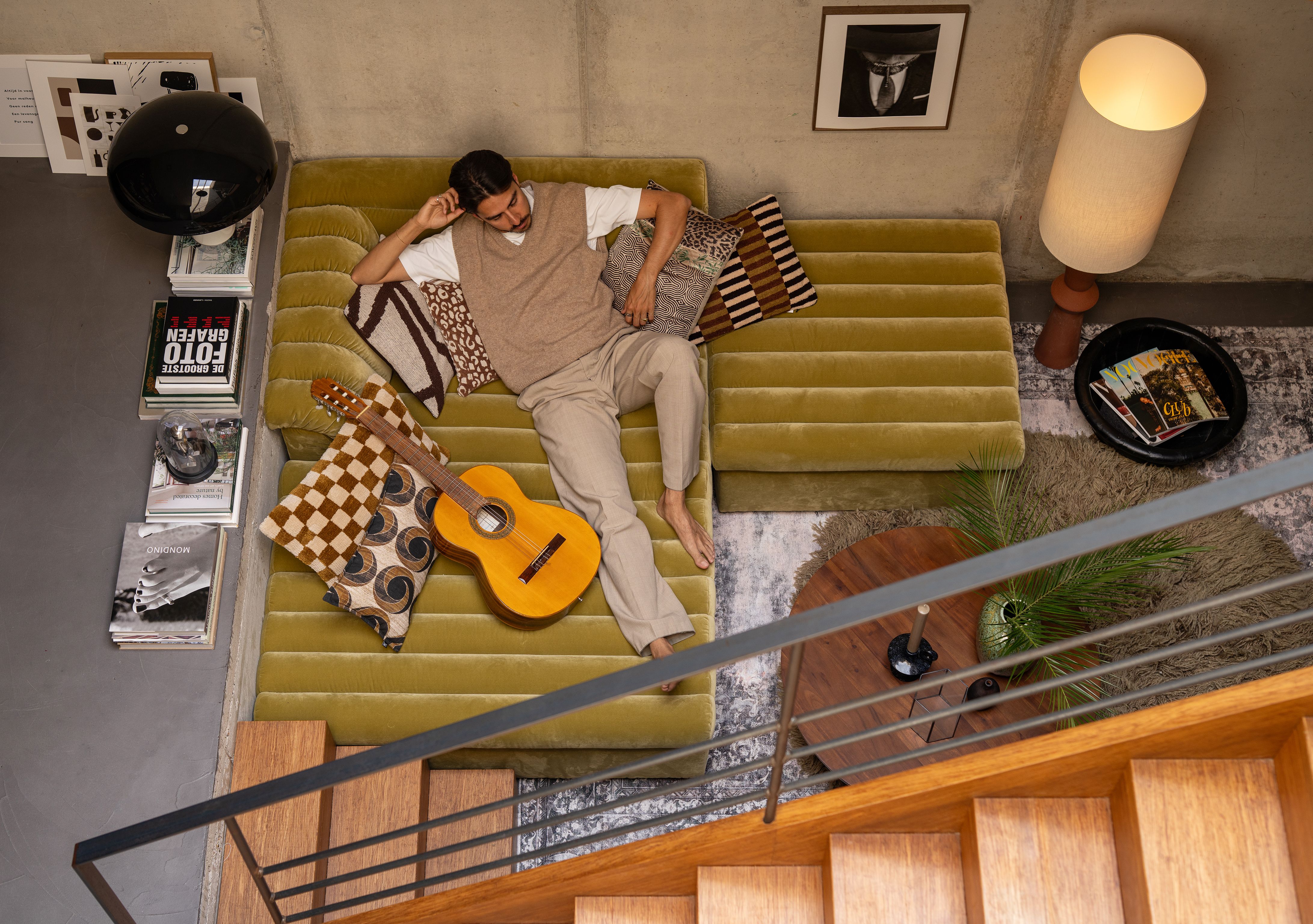 man ligt op groene bank met gitaar
