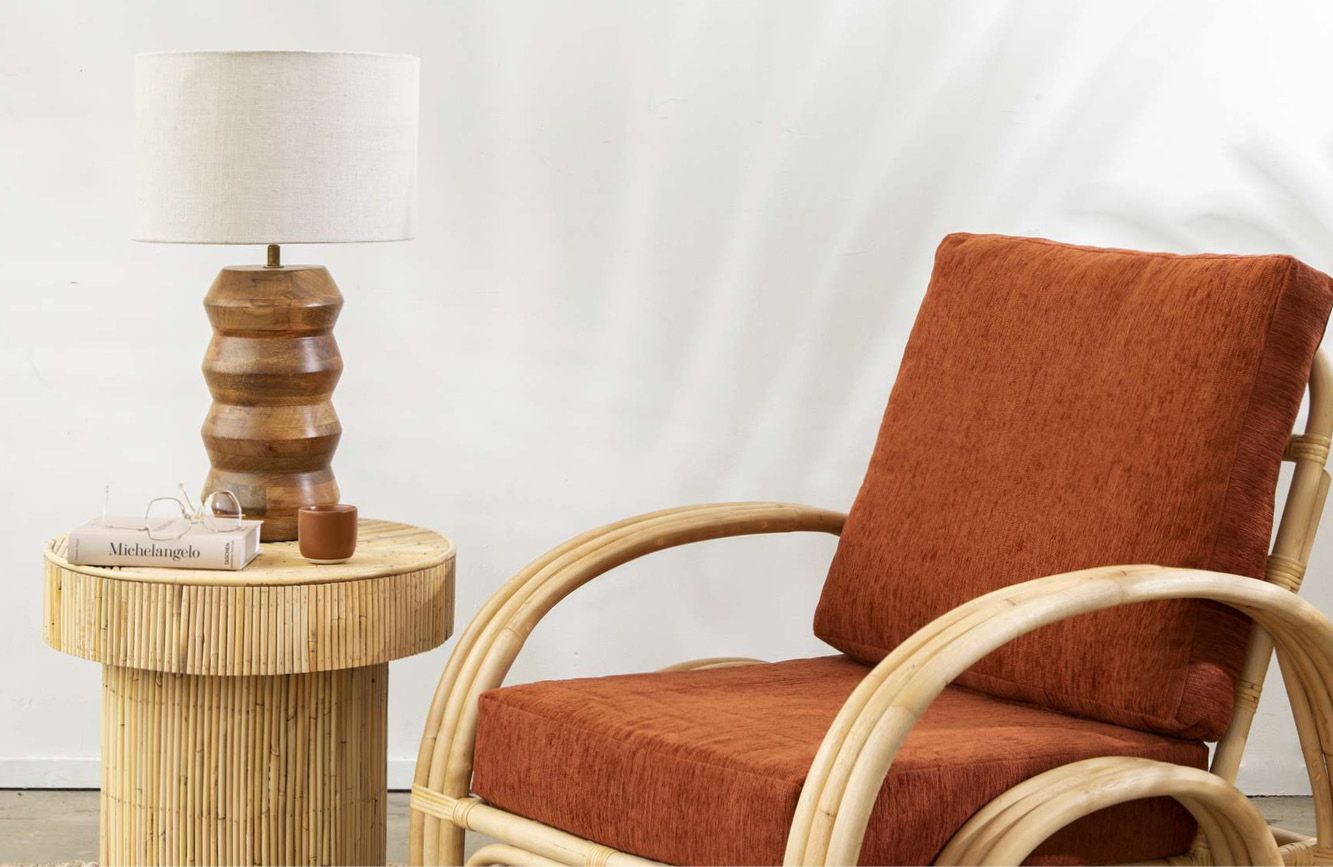 Houten lampenvoet op tafel met een fauteuil er naast