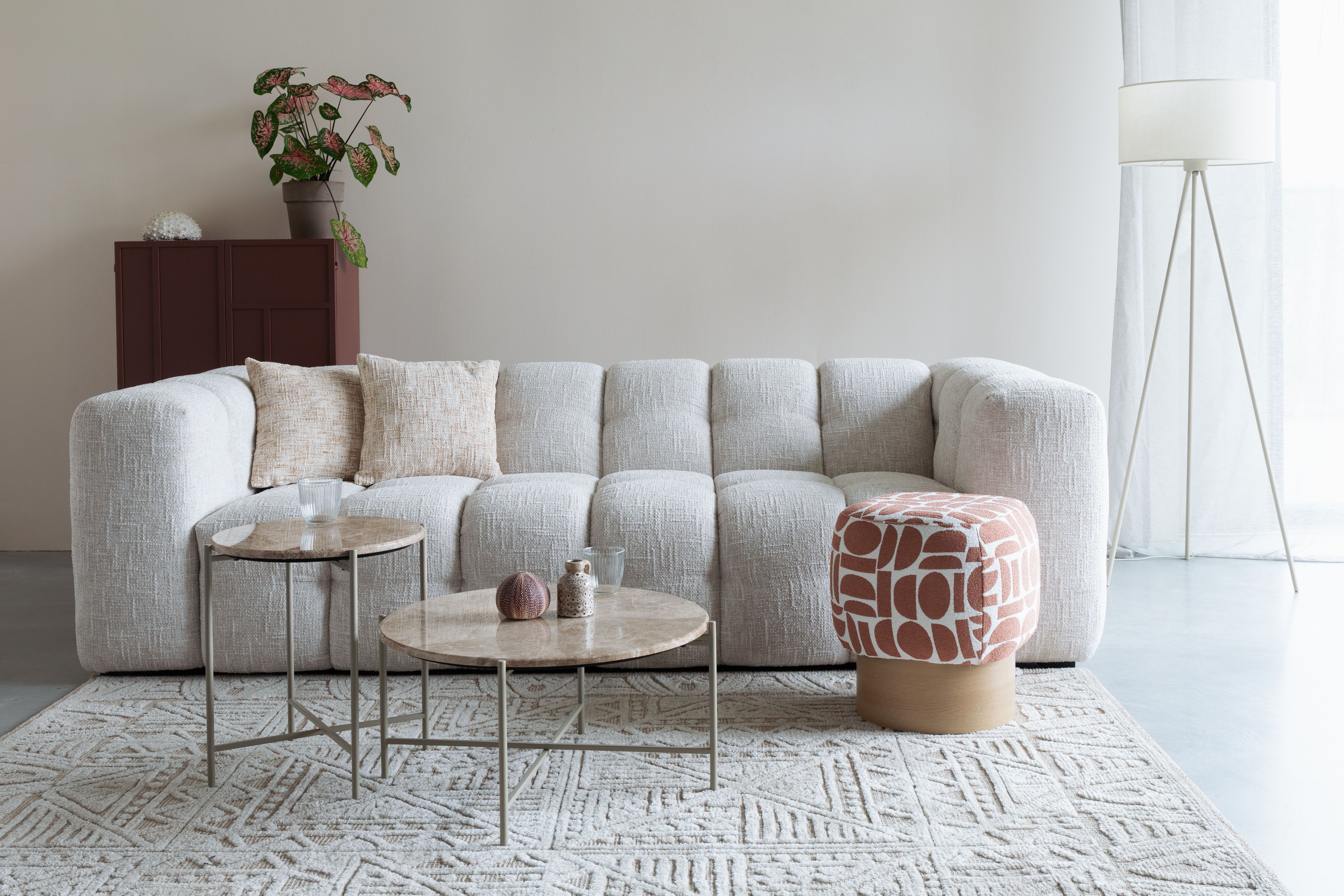 Beige bank in witte woonkamer met poef en salontafel