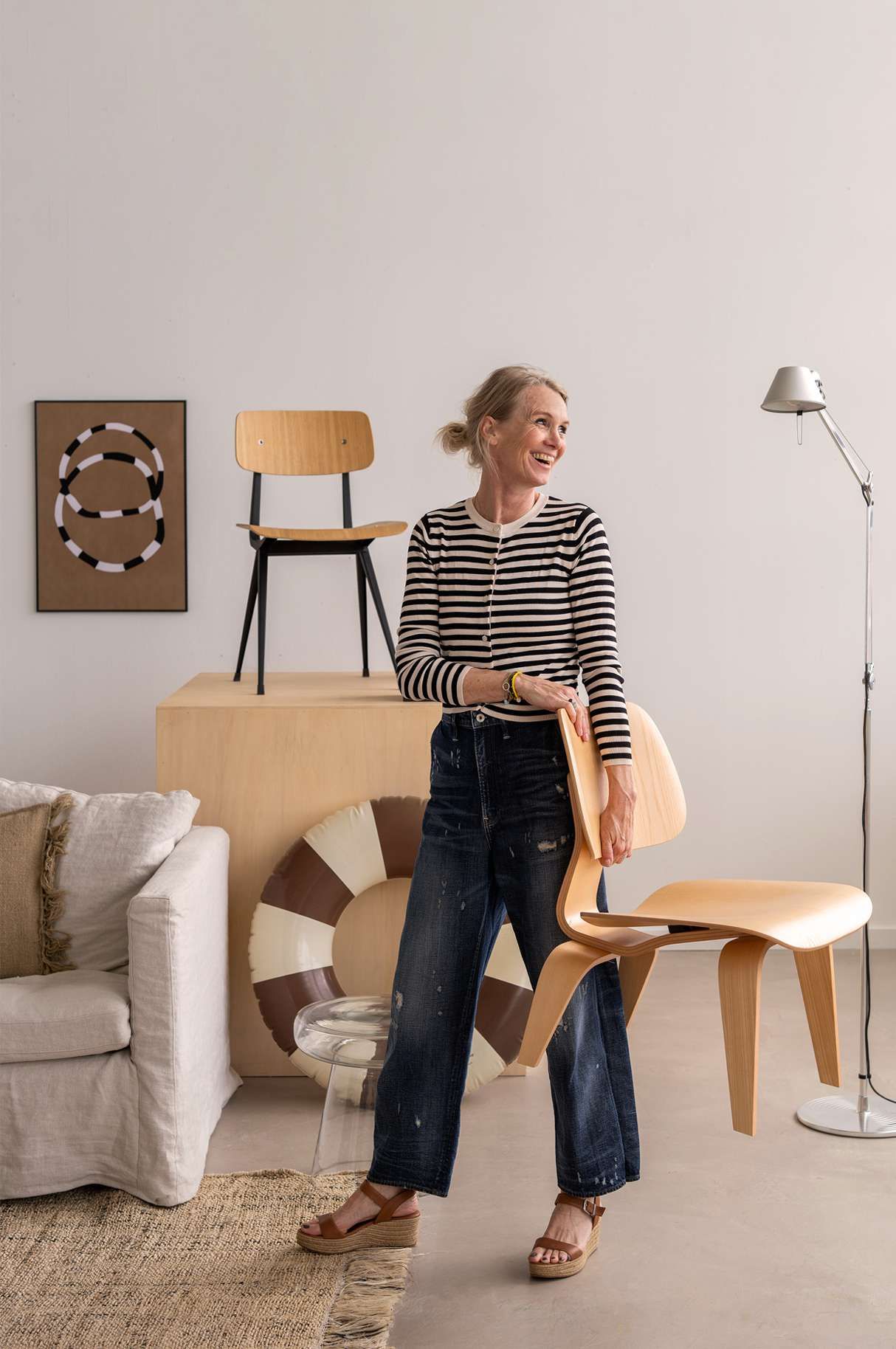 Vrouw in gestreept shirt tussen zomerse interieur items en houdt stoel vast
