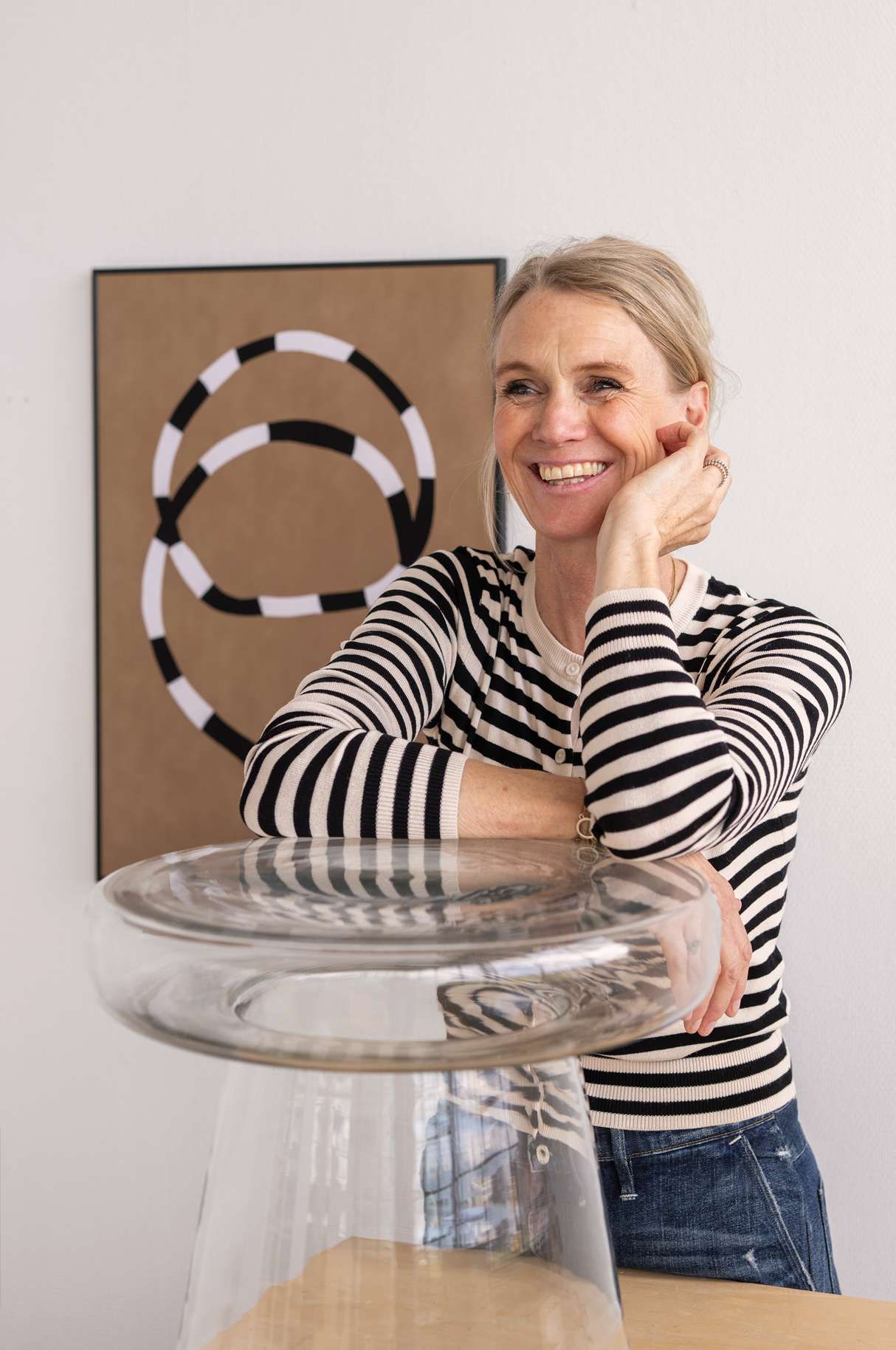 Blonde vrouw met gestreept shirt die leunt op transparante glazen bijzettafel