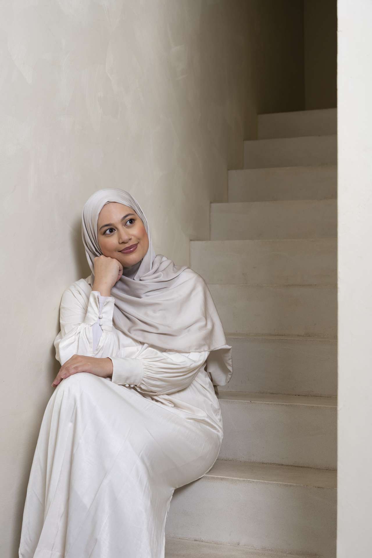 Vrouw met hoofddoek en witte jurk zit op trap
